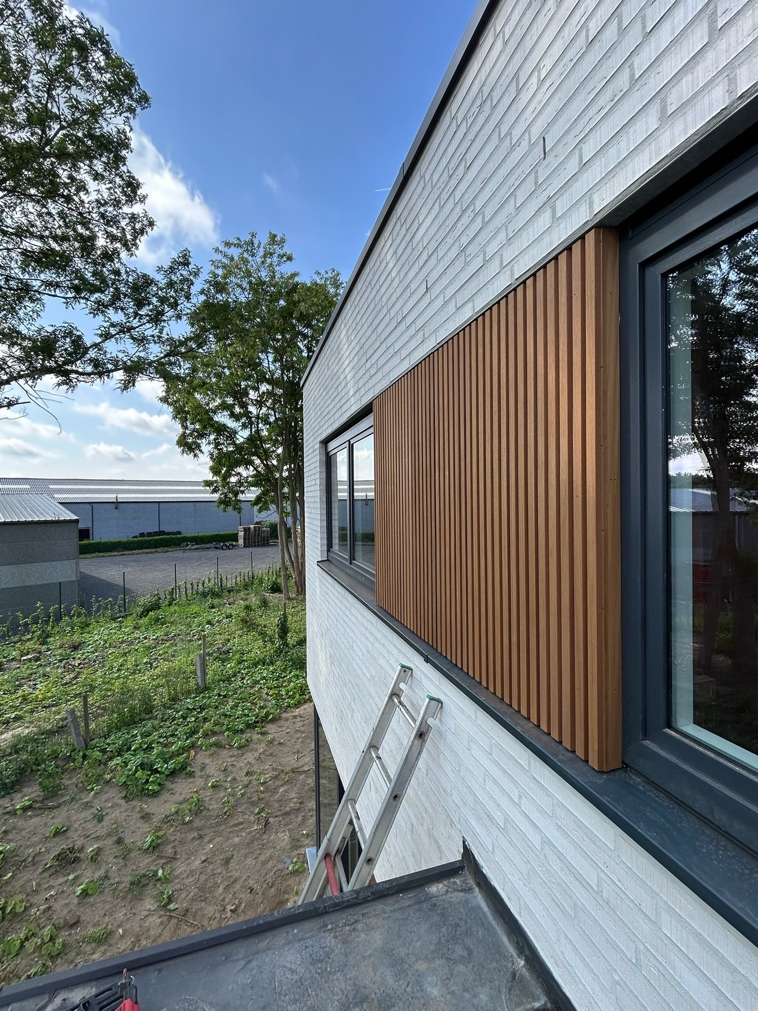 Houten lattenbekleding strak rond een raam in een witte gevel in Beernem