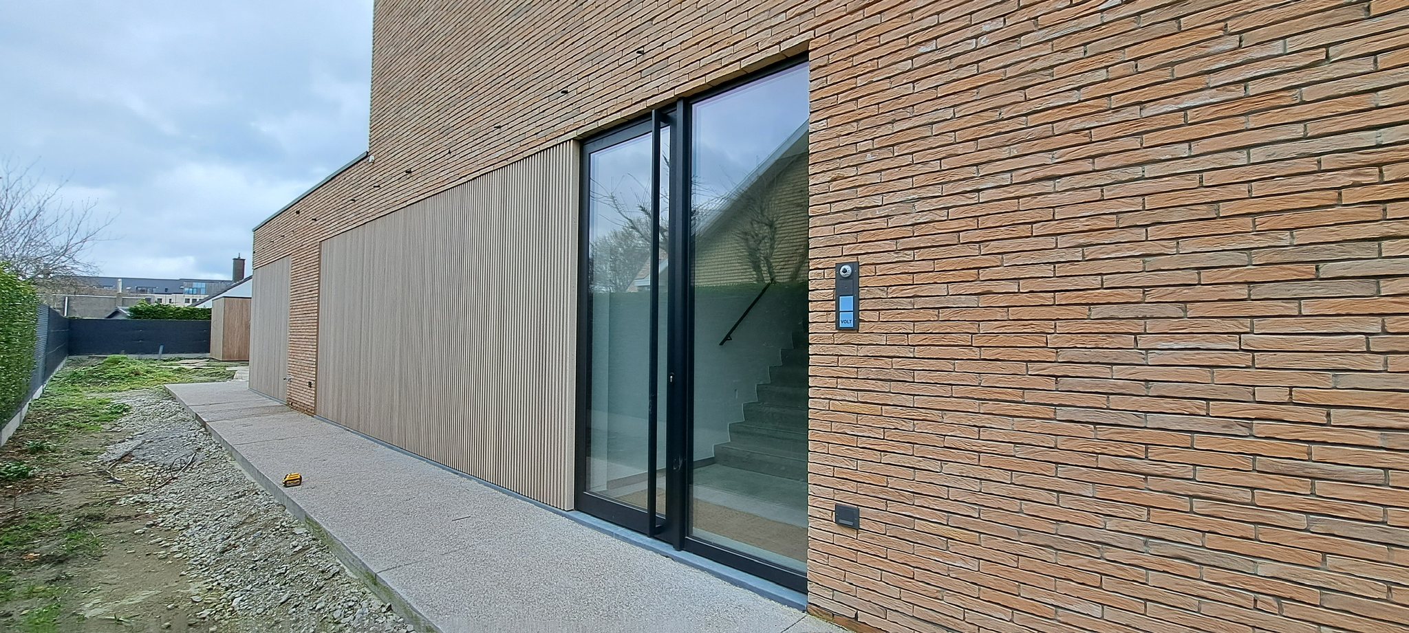 Nieuwbouw met verticale houten gevelbekleding naast baksteen en een glazen schuifraam in Zeebrugge