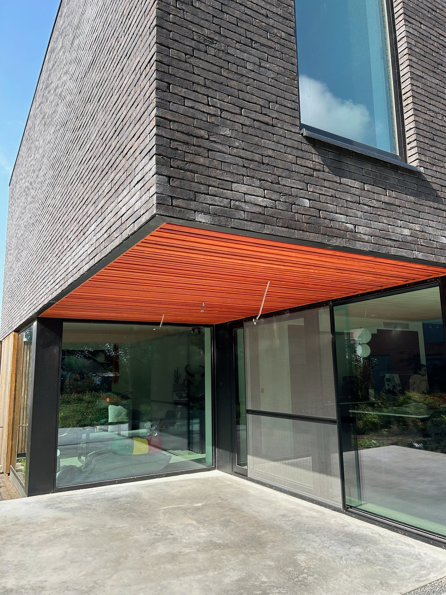 Rood houten plafond onder een overkapping boven een glazen gevel in Wintam