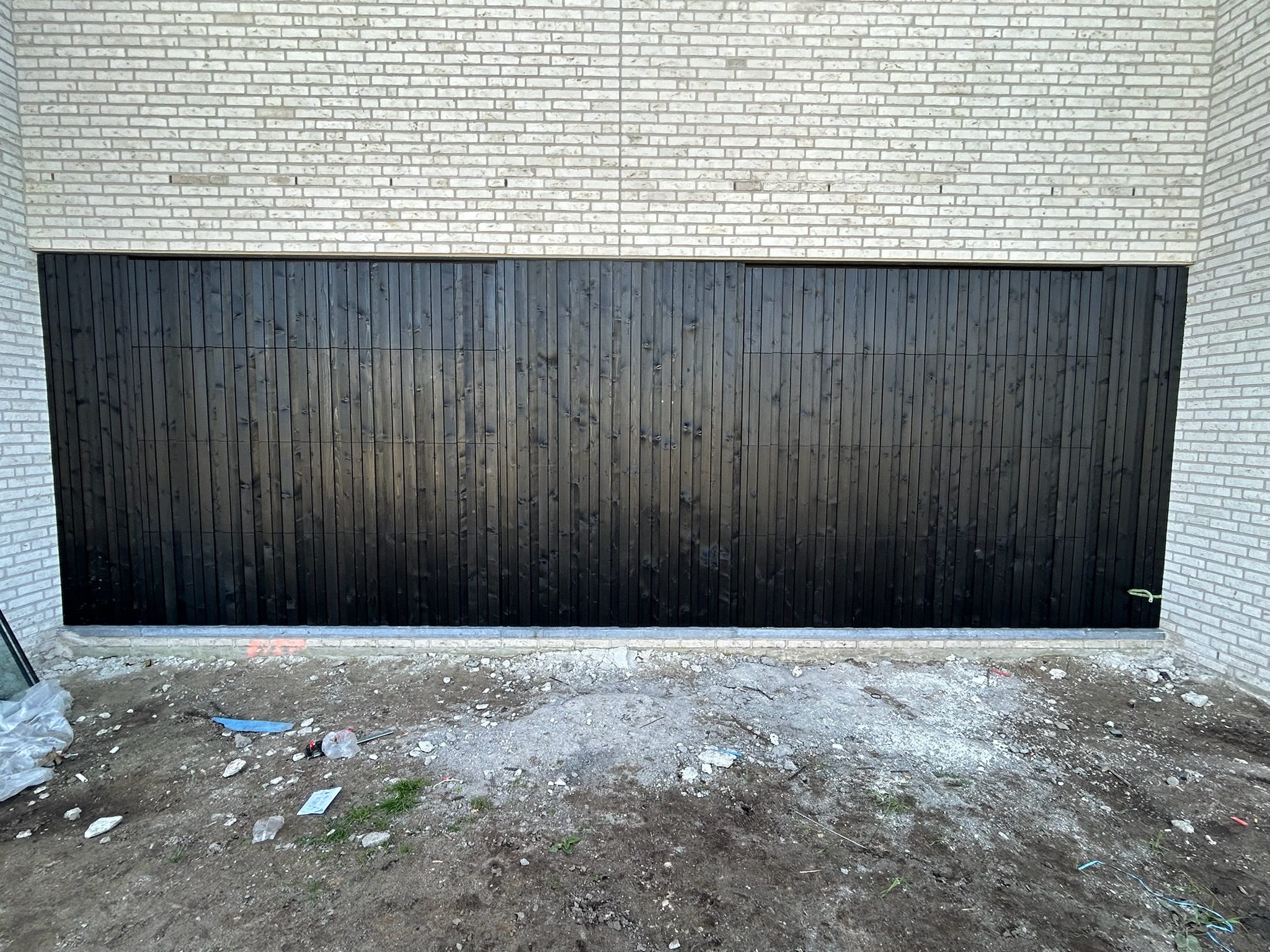 Zwarte houten gevelbekleding tussen witte baksteen in Rieme
